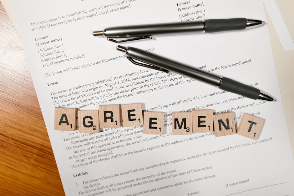 A document with Scrabble tiles spelling ‘AGREEMENT’ and two pens, symbolizing contract signing.